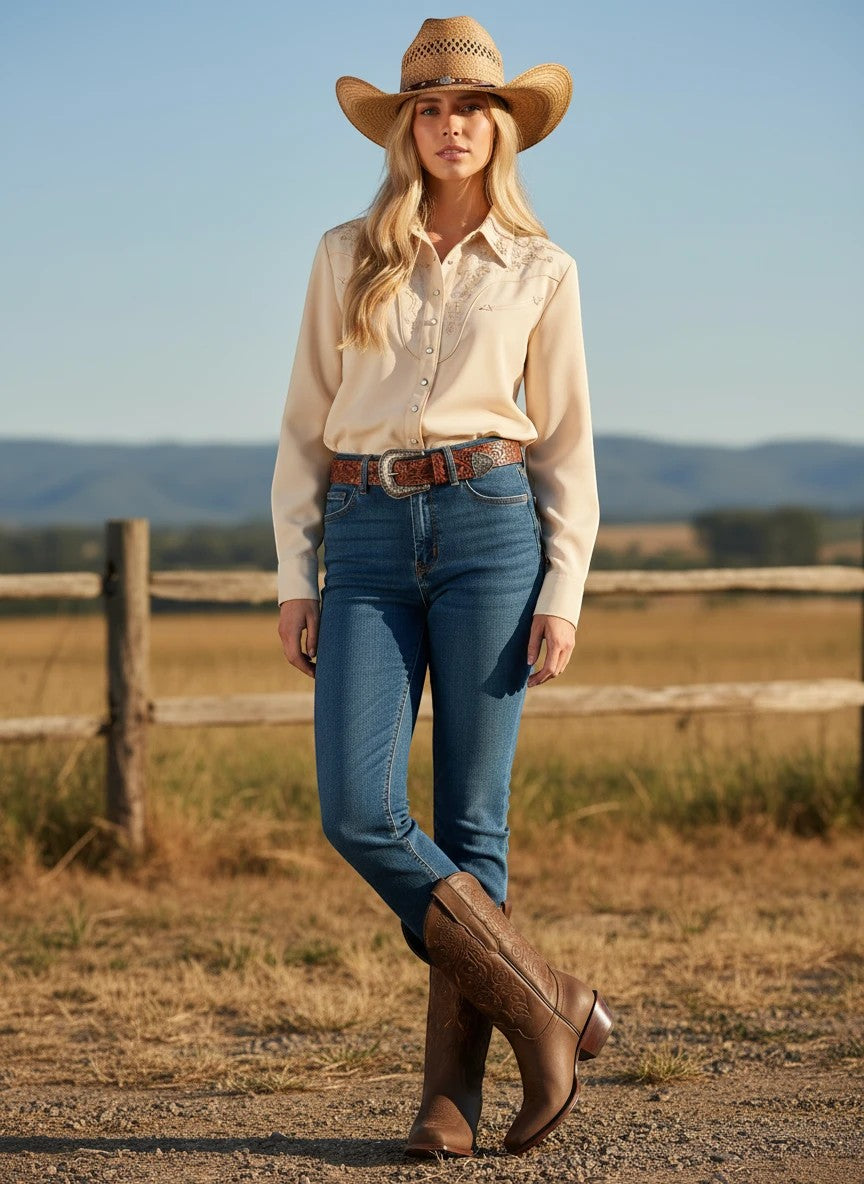 Mujer con botas vaqueras RAVAC de piel nobuck color camel, estilo western en entorno rural con sombrero y camisa