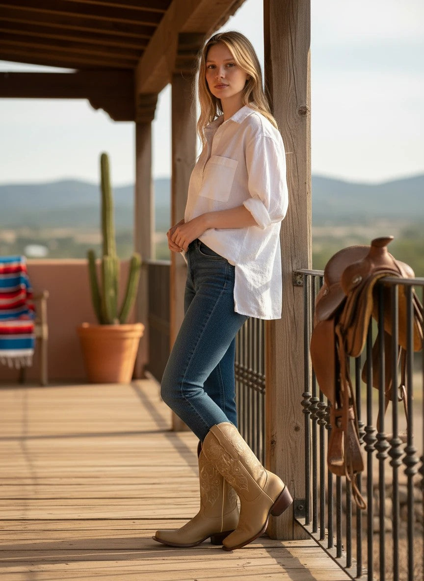 Mujer con botas vaqueras RAVAC de piel crazy en tono beige con bordados, estilo western en terraza rústica